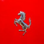 Close-up of a luxury car emblem on a glossy red surface displaying elegance and style.